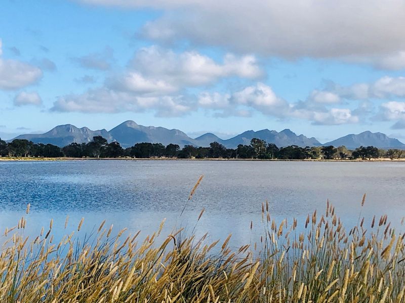 beautiful scenic photo showing grassland, water, mountains in the distance with blue sky and fluffy clouds