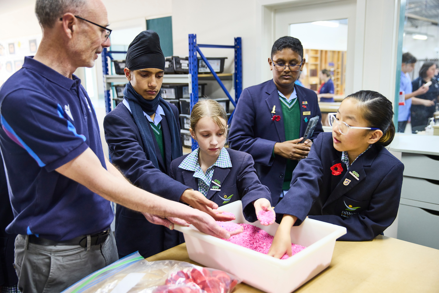 Teacher allowing students to put their hands in container with pink crystals