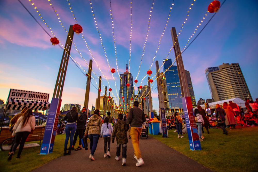 Crowd walking through a night market at dusk with a city skyline