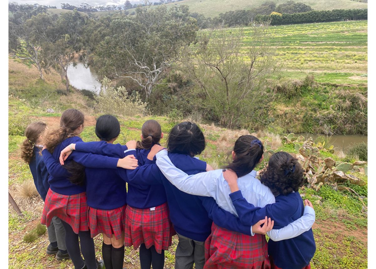 Group of school kids arm in arm looking over creek and bush land