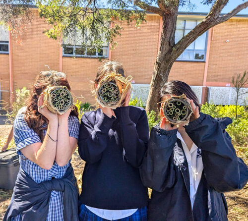 3 students holding bee hotels in front of their faces